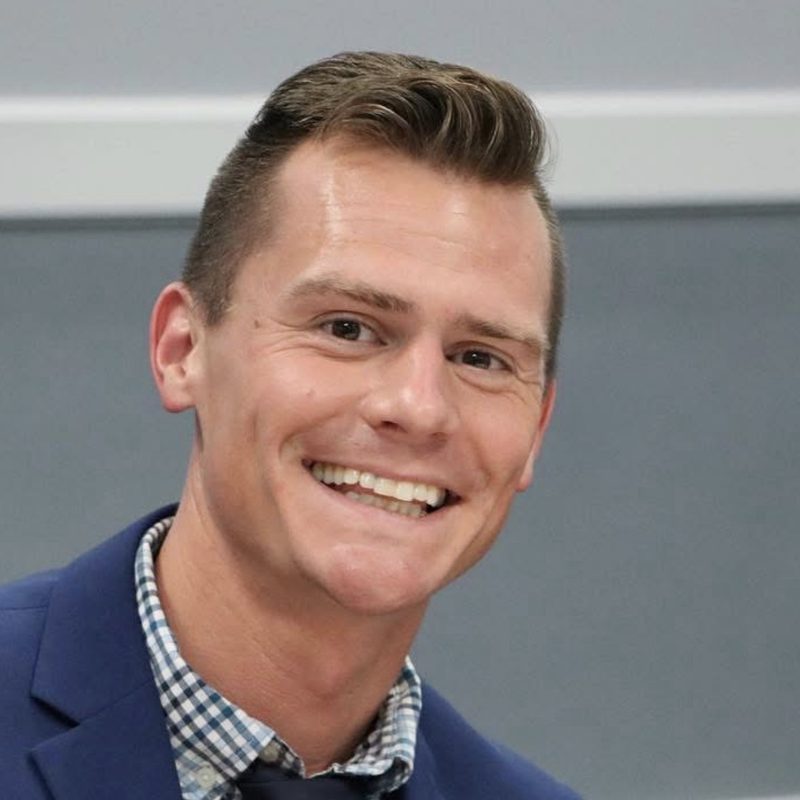 Taylor Clements, PhD, smiling, in a blue blazer